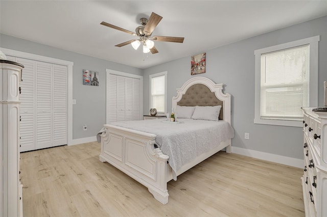 bedroom with multiple windows, multiple closets, ceiling fan, and light hardwood / wood-style flooring