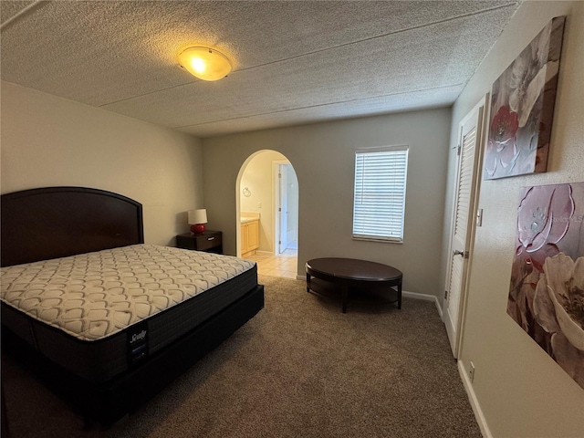 bedroom featuring ensuite bathroom, light carpet, and a textured ceiling