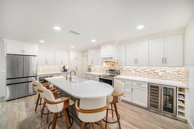 kitchen with appliances with stainless steel finishes, sink, white cabinets, wine cooler, and a kitchen breakfast bar