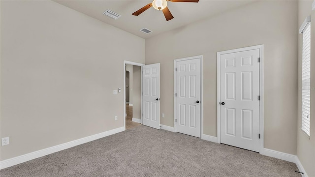 unfurnished bedroom with multiple closets, light colored carpet, and ceiling fan