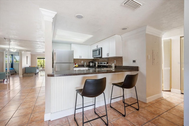 kitchen featuring light tile patterned floors, kitchen peninsula, white cabinets, stainless steel appliances, and backsplash