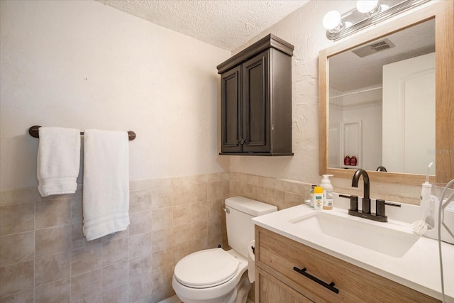 bathroom featuring vanity, tile walls, toilet, and a textured ceiling