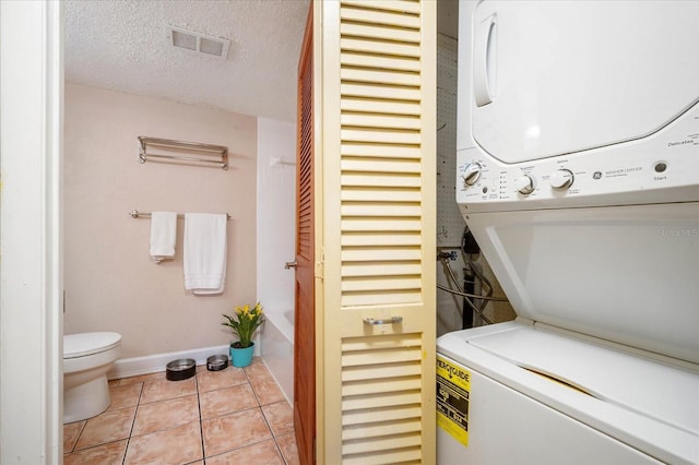 washroom featuring stacked washer and dryer, a textured ceiling, and light tile patterned floors