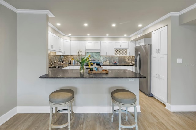 kitchen featuring appliances with stainless steel finishes, a breakfast bar, white cabinets, light hardwood / wood-style floors, and kitchen peninsula