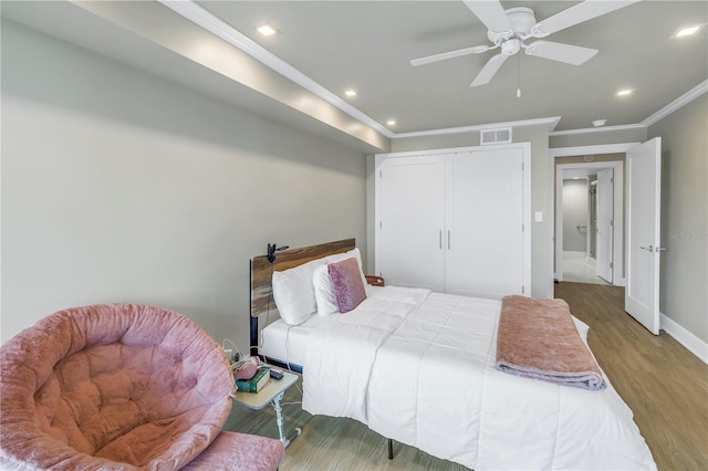 bedroom featuring ceiling fan, ornamental molding, wood-type flooring, and a closet