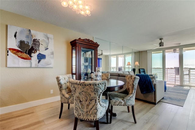 dining room with ceiling fan with notable chandelier, a wall of windows, a textured ceiling, and light wood-type flooring