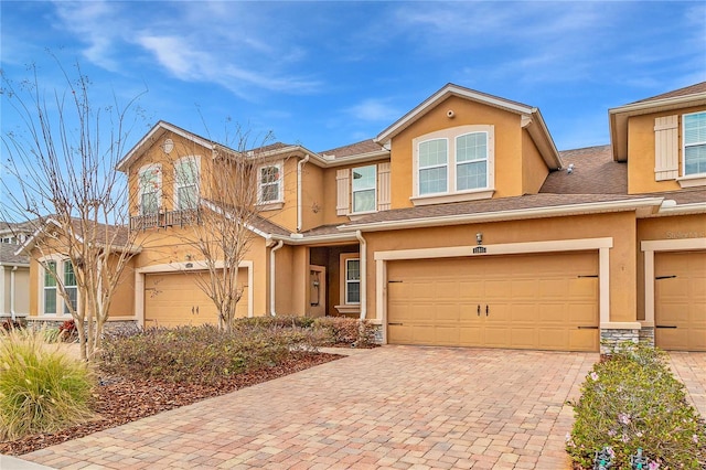 townhome / multi-family property with stucco siding, a garage, decorative driveway, and stone siding