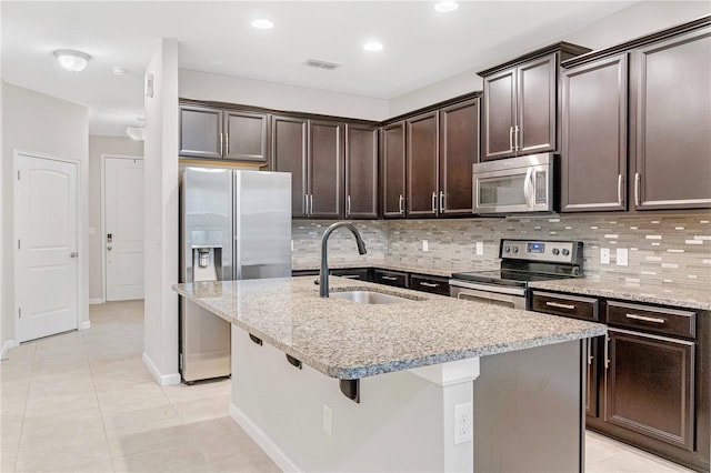 kitchen featuring stainless steel appliances, a sink, dark brown cabinetry, decorative backsplash, and light tile patterned floors