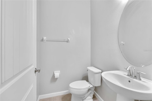 half bathroom with a sink, toilet, baseboards, and tile patterned floors