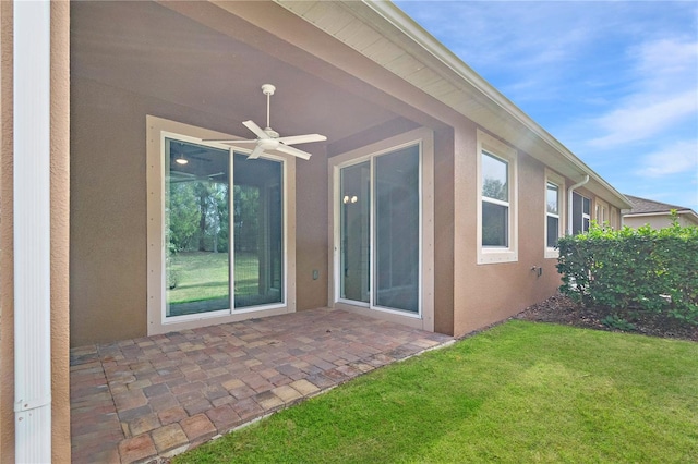 back of property with ceiling fan, stucco siding, a lawn, and a patio