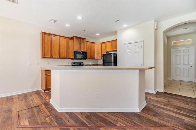 kitchen featuring dark hardwood / wood-style flooring, a center island with sink, and black appliances