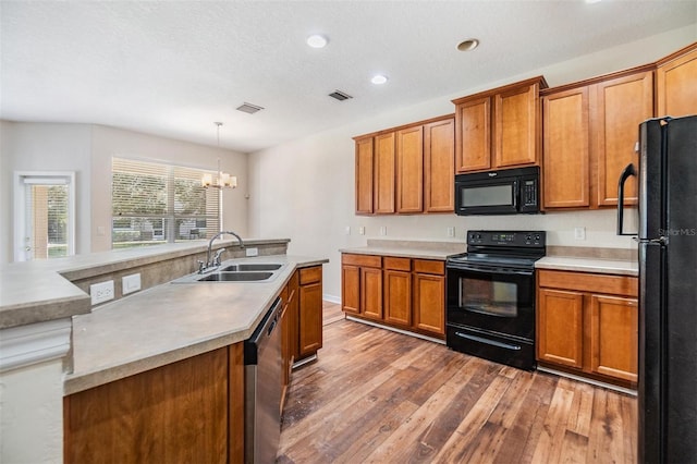 kitchen featuring sink, a chandelier, hanging light fixtures, black appliances, and light wood-type flooring