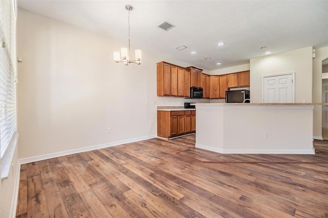 kitchen with pendant lighting, a chandelier, dark hardwood / wood-style flooring, a kitchen island with sink, and black appliances