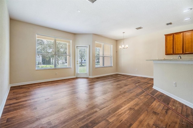 unfurnished living room featuring a textured ceiling, a notable chandelier, and dark hardwood / wood-style flooring