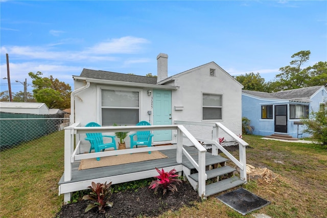 back of house featuring fence, a wooden deck, stucco siding, a chimney, and a yard