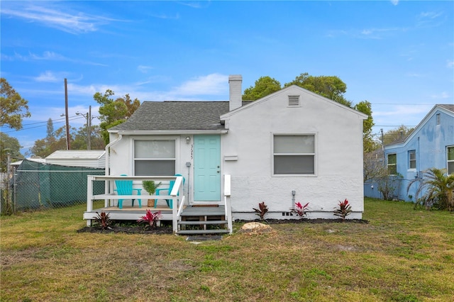 bungalow-style house with a shingled roof, a front lawn, fence, stucco siding, and a chimney