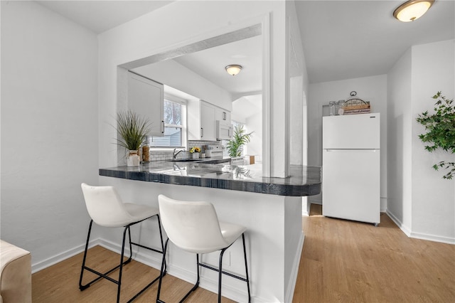 kitchen featuring sink, white appliances, a breakfast bar, white cabinetry, and kitchen peninsula