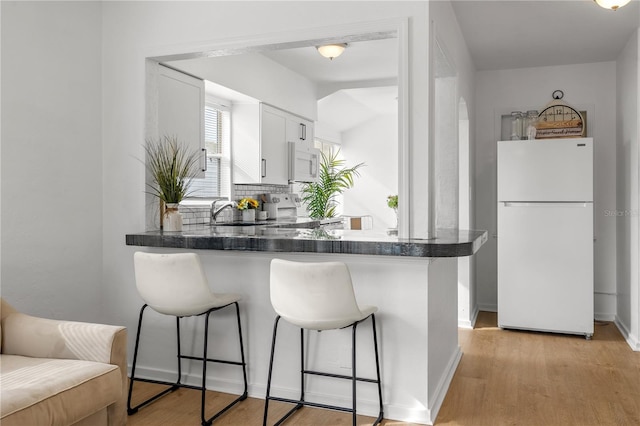 kitchen with white appliances, light hardwood / wood-style flooring, white cabinets, a kitchen bar, and kitchen peninsula