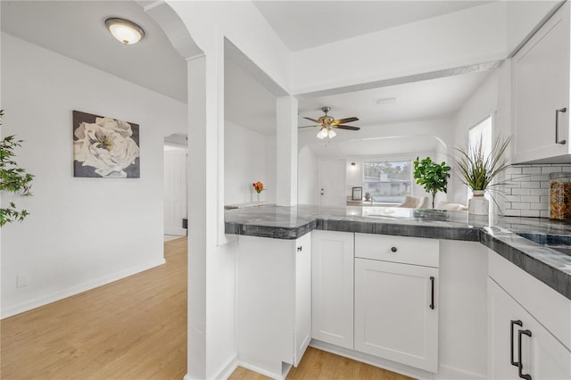 kitchen featuring white cabinetry, decorative backsplash, ceiling fan, kitchen peninsula, and light wood-type flooring