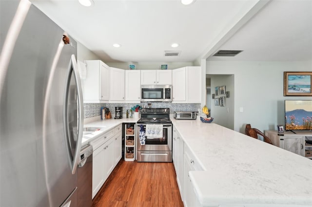 kitchen featuring white cabinetry, backsplash, hardwood / wood-style flooring, kitchen peninsula, and stainless steel appliances