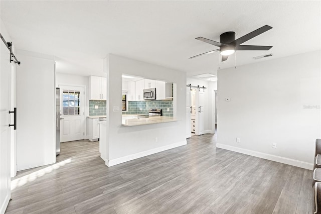 unfurnished living room featuring a barn door, ceiling fan, and light hardwood / wood-style floors