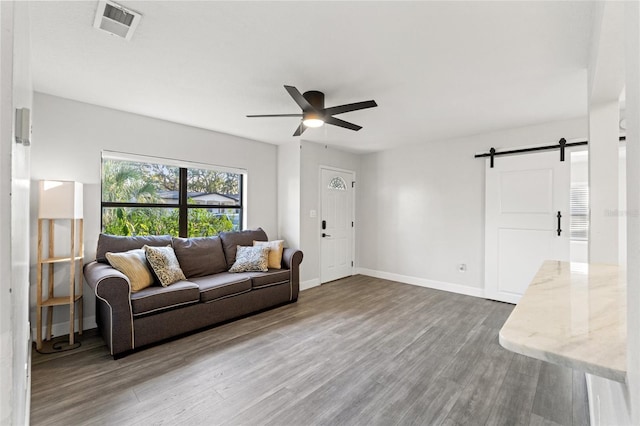 living room with wood-type flooring, a barn door, and ceiling fan