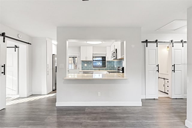 kitchen featuring appliances with stainless steel finishes, white cabinets, decorative backsplash, kitchen peninsula, and a barn door