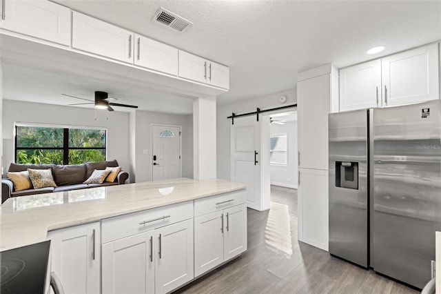 kitchen featuring white cabinetry, a barn door, stainless steel fridge, and ceiling fan