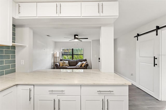 kitchen with light stone countertops, a barn door, white cabinets, and kitchen peninsula