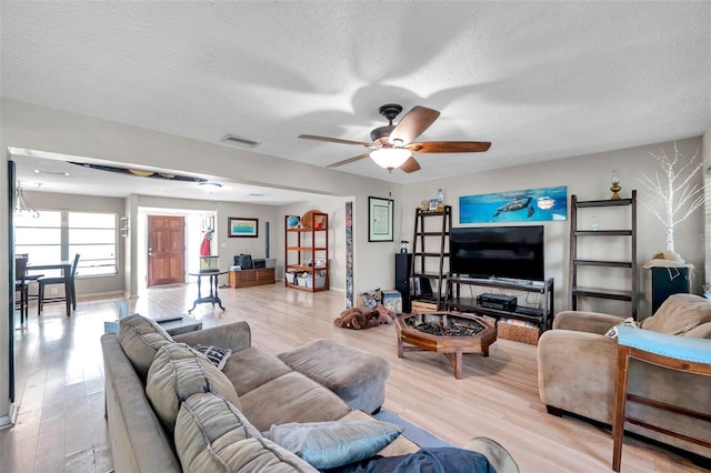 living room with a textured ceiling, ceiling fan, and light hardwood / wood-style flooring