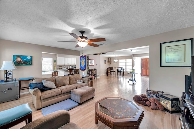 living room featuring ceiling fan, a textured ceiling, and light wood-type flooring