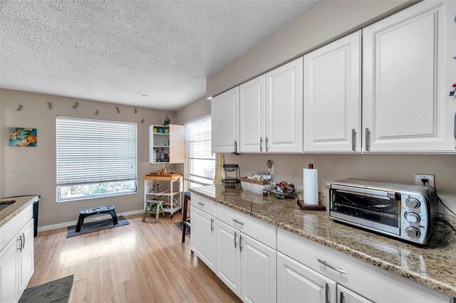 kitchen featuring white cabinetry, light wood-type flooring, a textured ceiling, and light stone counters