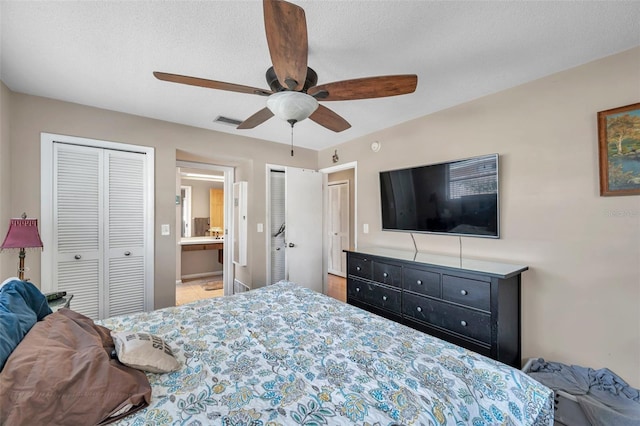 bedroom featuring ceiling fan, ensuite bath, a textured ceiling, and two closets