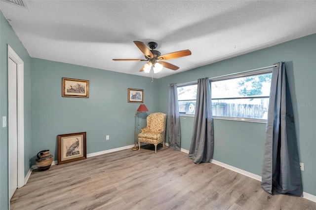 living area with ceiling fan, light hardwood / wood-style floors, and a textured ceiling