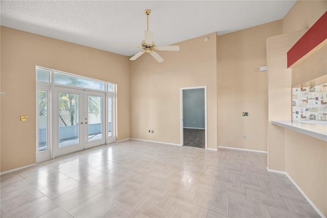 empty room featuring french doors, a towering ceiling, ceiling fan, and a textured ceiling