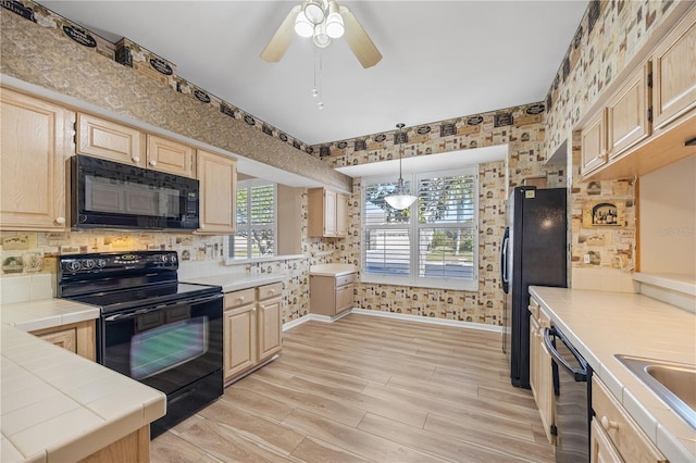 kitchen featuring hanging light fixtures, tile countertops, light brown cabinetry, and black appliances