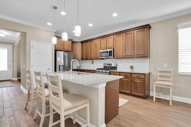 kitchen with sink, light stone counters, decorative light fixtures, appliances with stainless steel finishes, and an island with sink