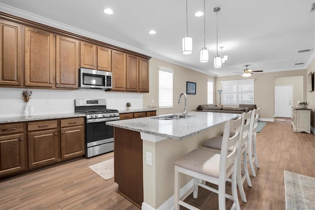 kitchen featuring sink, a breakfast bar area, light stone counters, appliances with stainless steel finishes, and a kitchen island with sink