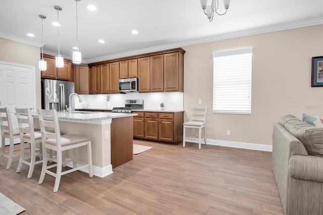 kitchen featuring sink, appliances with stainless steel finishes, a kitchen island with sink, hanging light fixtures, and a kitchen breakfast bar