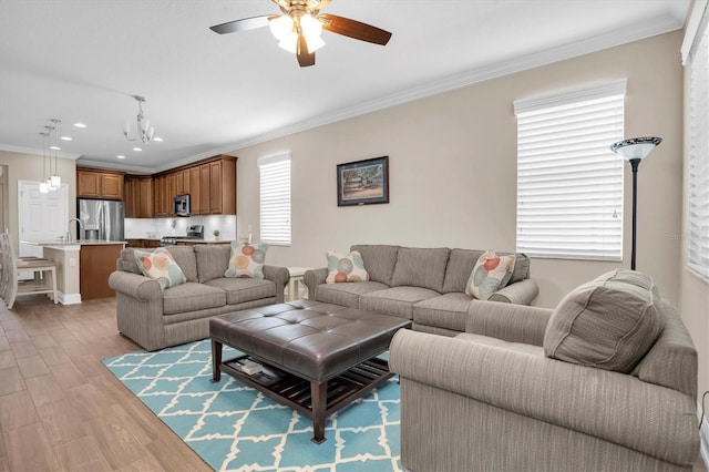 living room featuring crown molding, ceiling fan with notable chandelier, and light wood-type flooring