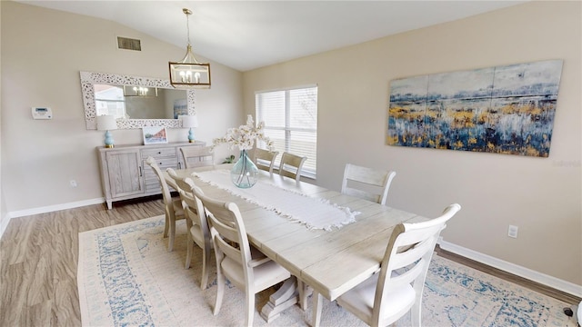 dining space featuring an inviting chandelier, vaulted ceiling, and light wood-type flooring