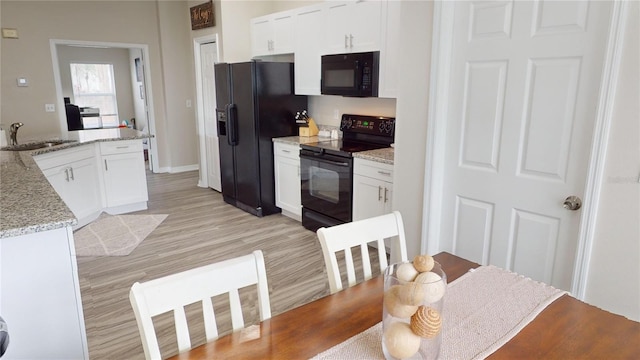 kitchen featuring sink, white cabinetry, light stone counters, light hardwood / wood-style floors, and black appliances