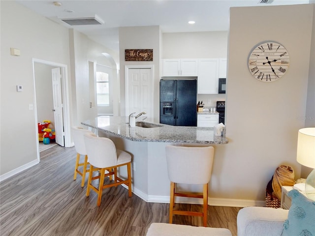 kitchen featuring sink, white cabinets, a kitchen bar, light stone counters, and black appliances