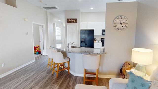 kitchen featuring sink, white cabinetry, a kitchen breakfast bar, light stone countertops, and black appliances