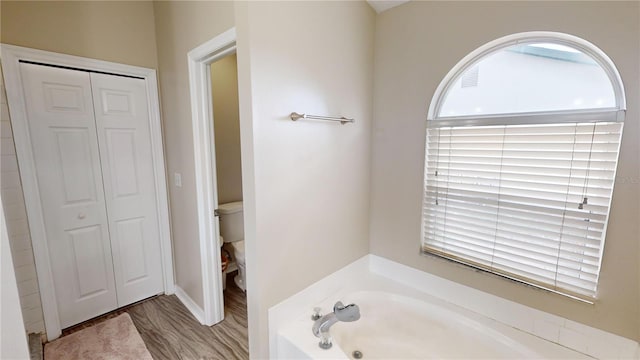 bathroom featuring toilet, hardwood / wood-style floors, and a tub to relax in