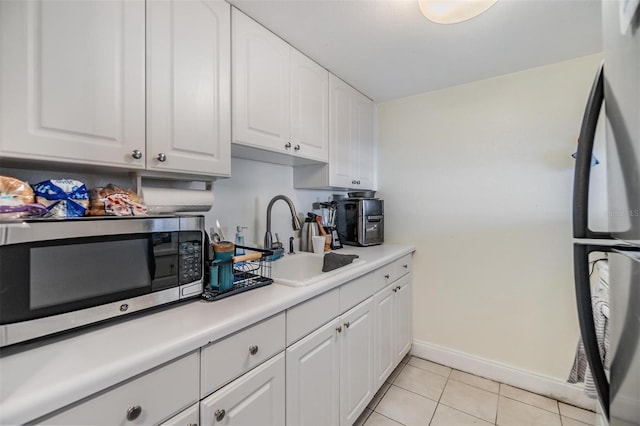 kitchen featuring black refrigerator, sink, white cabinets, and light tile patterned flooring