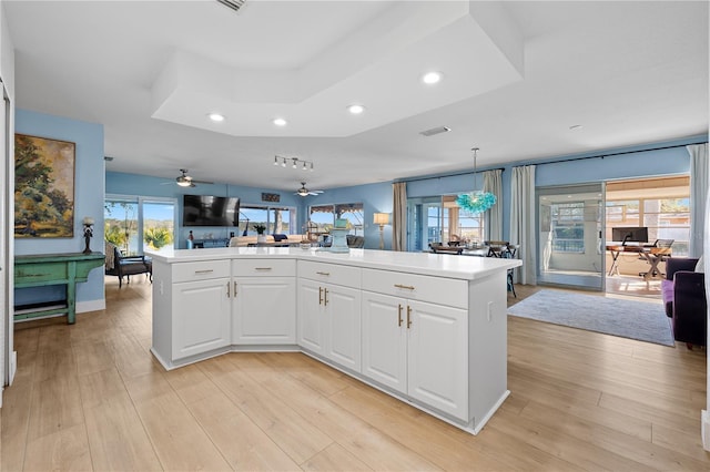 kitchen featuring decorative light fixtures, white cabinetry, a center island, a tray ceiling, and light wood-type flooring