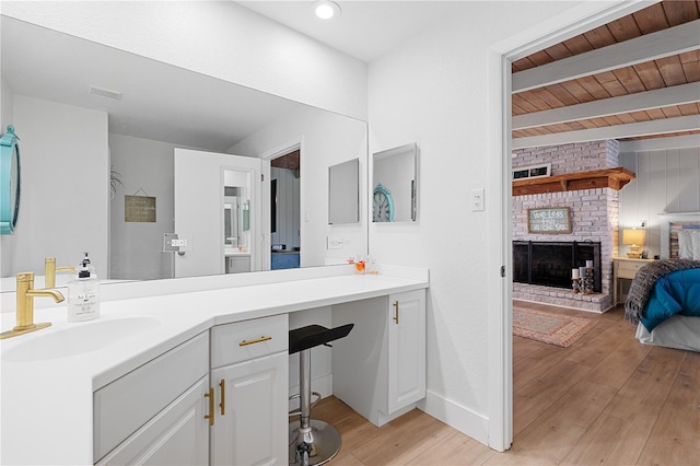 bathroom with beamed ceiling, hardwood / wood-style flooring, vanity, wood ceiling, and a brick fireplace