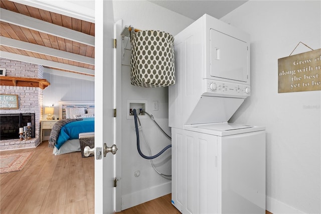 laundry room featuring stacked washer / drying machine, wood ceiling, a fireplace, and light hardwood / wood-style floors