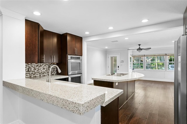 kitchen with sink, appliances with stainless steel finishes, tasteful backsplash, dark hardwood / wood-style flooring, and kitchen peninsula